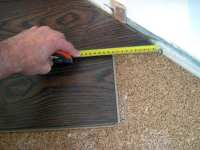 Прежде, чем обрезать край ламинатной доски, необходимо точно измерить расстояние от ламинатного ряда до распорных колышек